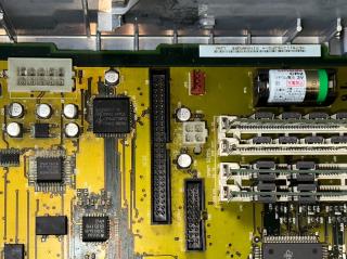Close-up PowerMac 7100 motherboard with corrosion on the pins of the surface mount chips near some surface mount capacitors. Also visible is a CR2 3V Lithium 1/2AA barrel battery with Japanese print on it.