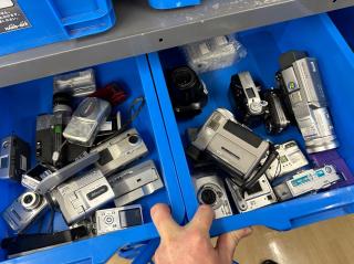 Blue bins full of point & shoot cameras and handycams, that all look in terrible condition.