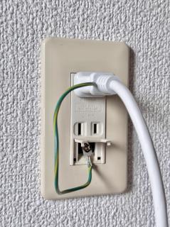 A plug in a wall socket. The outlet has two US-style two-prong outlets, except under them there is a ground screwed with the aforementioned ground wire screwed in