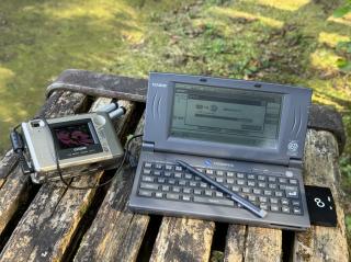 A digital camera and a handheld PC, with the handheld PC showing a transfer in progress