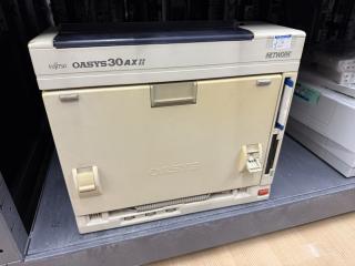 A standing square beige box with Fujitsu OASYS30AXii Network printed on it. On the right are two floppy drives.