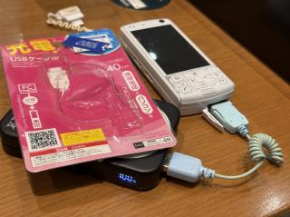 An old feature phone connected to a mobile battery bank and the package for the cable
