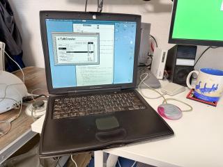 A PowerBook G3 Lombard with a pink puck mouse A PowerBook 540c is seen in the background Off the the left, on a shaky camping table, an iMac G4 can be spotted