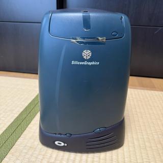 Front of a SGI O2, with a round teal appearance, cool 3D logo and an optical drive bay cover that is taped on with yellowing tape
