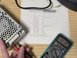 Power supply with a paper clip in two of the pins and a multimeter measuring two other pins