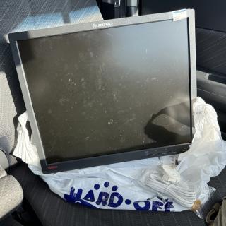 A black LCD monitor labeled Lenovo ThinkVision is perched in a car seat, on top of a plastic bag labeled HARD OFF. The monitor has a price tag that says 550 yen. There are also some RJ11 phone cables