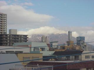 A photo of a snow-capped volcano in the distance with mid-rise buildings and power lines in the foreground 