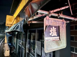 A sign saying 塩 / 塩事業センター指定契約 hanging from a rotting sunshade with a sun-faded tobacco sign in the background 