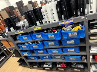 Racks of blue bins full of game controllers marked N64/GC, PS, PS2, SFC, WiiU