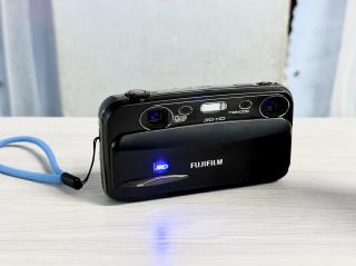 A 10 year old pocket camera from FUJIFILM with dual lenses and a blue glowing 3D logo