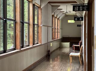 Hallway of old Japanese school building, with signs for 6年　5年　図書館 and greenery visible from the windows