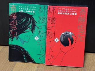 A green and a red book with a manga style drawing of Steve Jobs looking way cooler than he ever did in real life holding an Apple.The cover for each says 林檎の樹の下で (Under the Apple Tree)The red one says 上 (upper) with the subtitle 禁断の果実上陸編 (Landing of the forbidden fruit edition)The green one says 下 (lower) with the subtitle 日本への帰化編 (The naturalization to Japan edition)