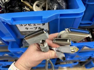 A handful of SCSI and serial cables in front of blue bins full of more cables and computer parts