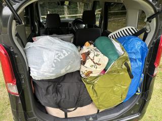The rear hatch of a kei micro minivan(?) stuffed to the gills with tent, camping gear, clothes, sleeping bags, etc.