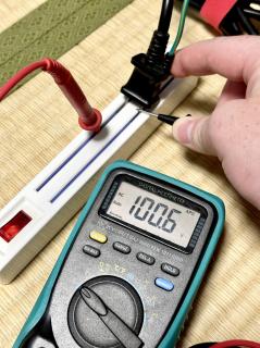 A plug half-plugged into the power strip, measuring 100V off the half-exposed pins