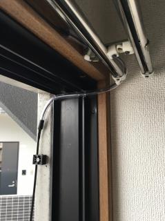 The aluminum frame of a balcony door with a hole drilled through the corner and a plastic tube with a fiber going through it