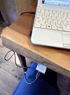 A white netbook on a wooden counter with an illuminated classic Mac face peeking out from underneath with a black usb c cable going to the netbook