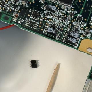 Top view of a Newton PCB. A chip has come off the board and is lying in the table. There is also a toothpick.