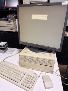 A photo of a Macintosh IIcx with keyboard and mouse and an LCD monitor ontop showing a Macintosh System 6 boot screen but instead of “Welcome to Macintosh” it says 「あけましておめでとうございます」