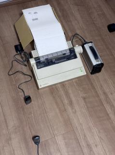 An ImageWriter II on the floor with an IR receiver pointed at another IR receiver. Two tractor feed prints have come out of it