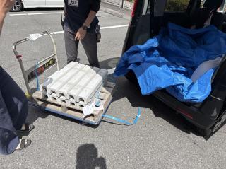 A trolley with 10 concrete U troughs on it and a small kei car