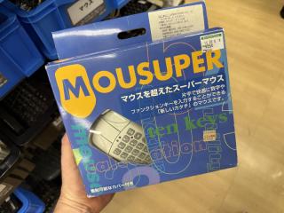 A box containing a mouse with a calculator's worth of buttons with numbers, F-numbers, Ctrl/Alt/Tab etc printed on themit saysマウスを超えたスーパーマウス片手で快適に数字やファンクションキーを入力することができる「新しいカタチ」のマウスです。