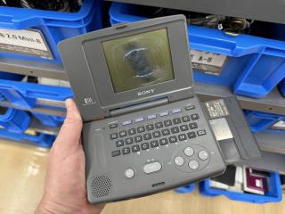 A clamshell device opened up to reveal a 4:3 black and white LCD where the polarizer has become delaminated. There is a rubber key QWERTY keyboard, big NO and YES keys, and a disc caddy sticking out the size.