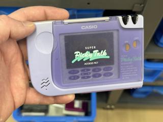A purple CASIO device with a clear plastic lid with teal script “Picky Talk” “ACCESS PET”