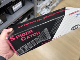 A box that says SPIDER CATCH, Non-Lethal Weapon, with an image of what looks like a beefy flash light projecting a grid