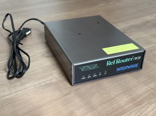 A small black and grey box on a table. It says Ref Router/TCP and INTERWARE. There is a stick on top with IP addresses. There are LED lights for PWR, RDY, ERR, ET, LT.