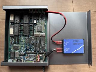 A device opened up to reveal a PCB on the bottom half and a metal lid with a TDK Power Supply FMP05-2R0 screwed to the top, with wires going from the AC cable to a header on the PCB.